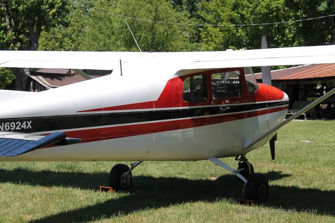 A side view of the red and white Cessna 172, showing the cockpit windows and tail section on a grassy field.