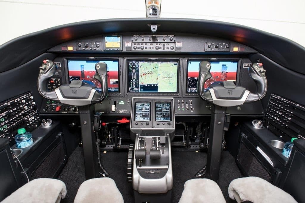 The modern cockpit of a business jet, featuring multiple large display screens and dual yokes.