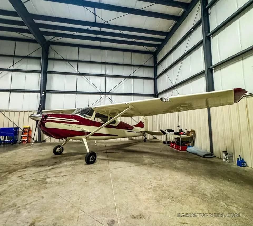 A full side view of a red and white single-engine propeller aircraft parked in a hangar.