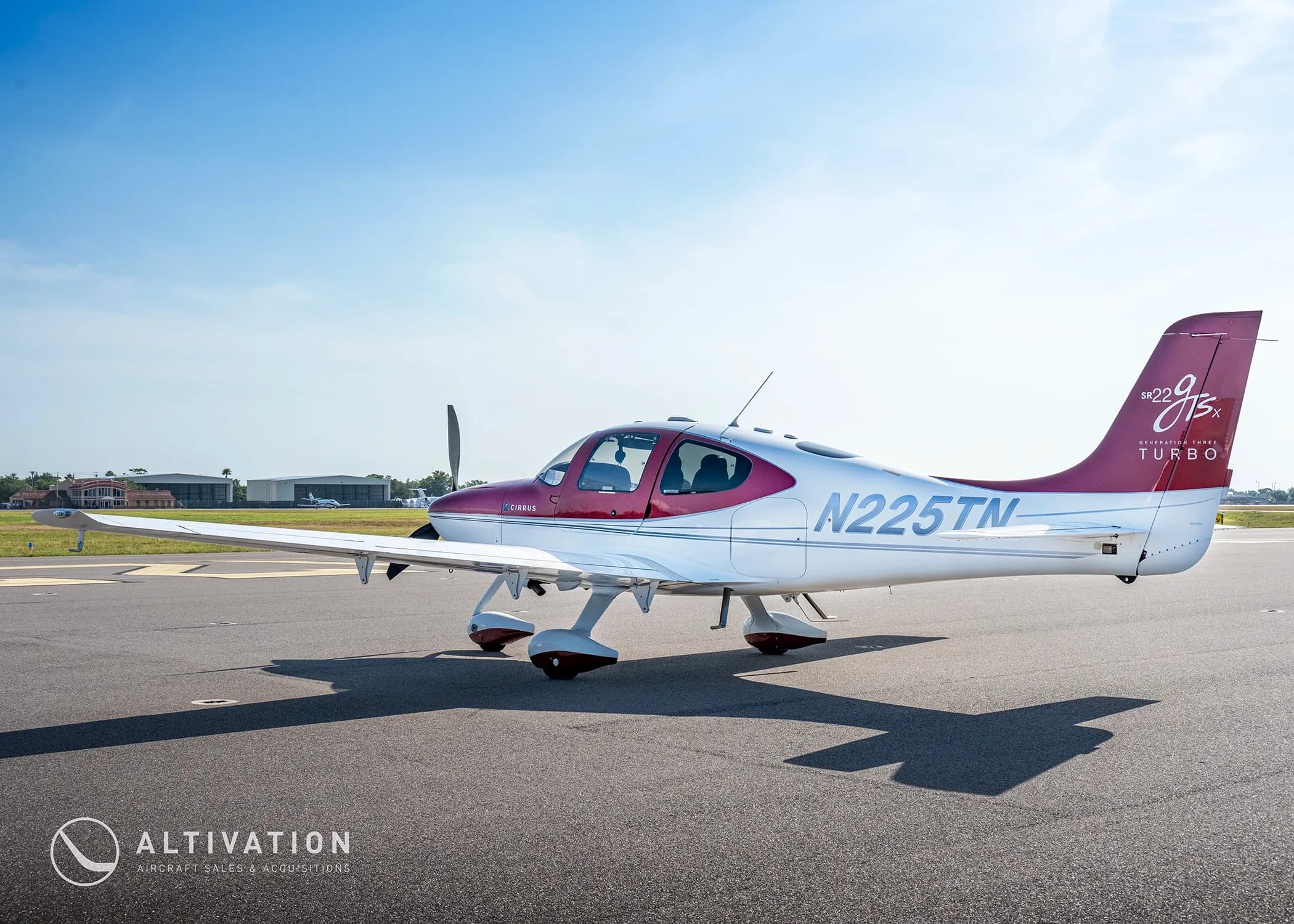 A rear three-quarter view of a red and white Cirrus SR22T aircraft (N225TN) parked on an airfield.