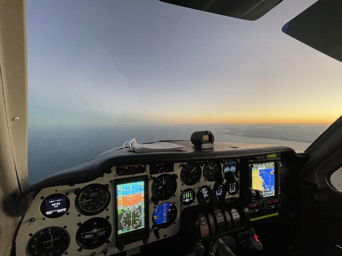 A view from the cockpit during flight, showing the instrument panel and a sunset over the horizon.