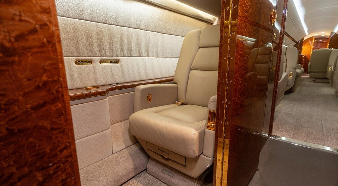 A luxurious aircraft interior with a single beige leather seat, polished wood paneling, and a carpeted floor.