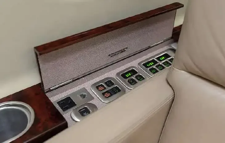 A close-up of the passenger control panel and cup holder integrated into the side console of an aircraft cabin.