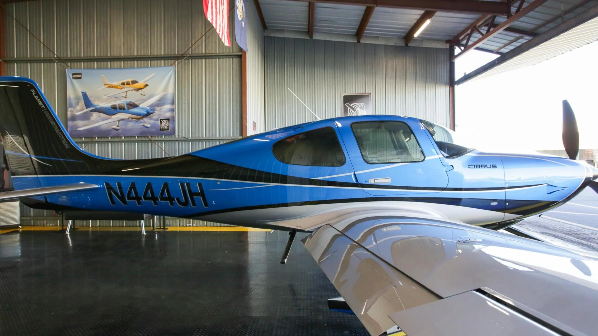 A close-up side view of the fuselage and wing of a blue and silver Cirrus SR22 aircraft with registration N444JH.