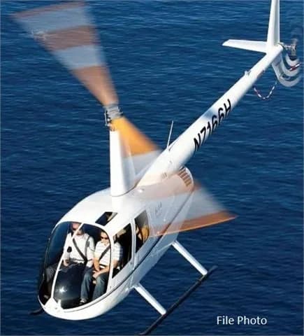 A white Robinson R44 helicopter flying over the ocean.