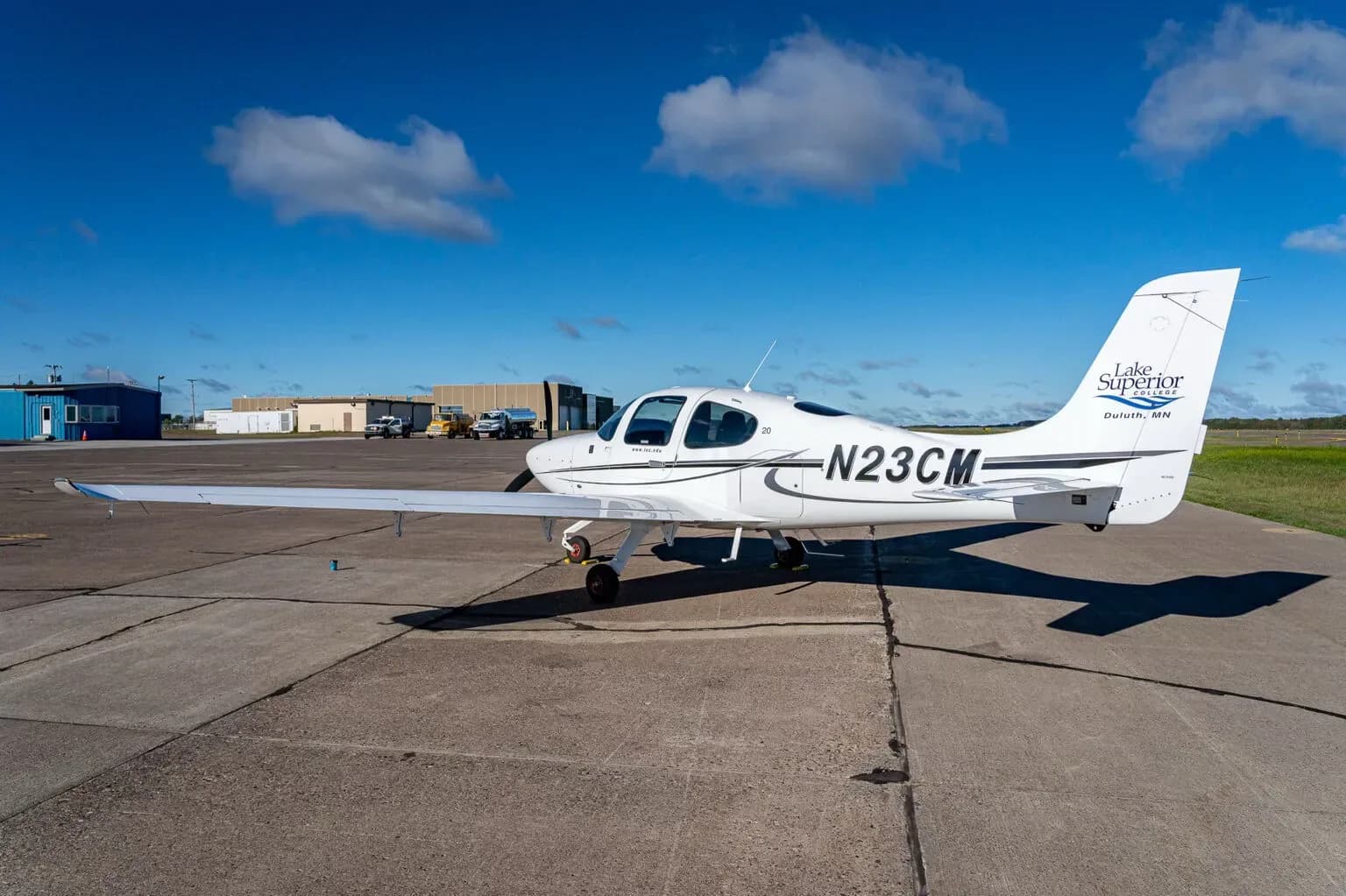 A white Cirrus SR20 aircraft with registration N23CM and "Lake Superior College" logo on the tail, parked on an airfield.