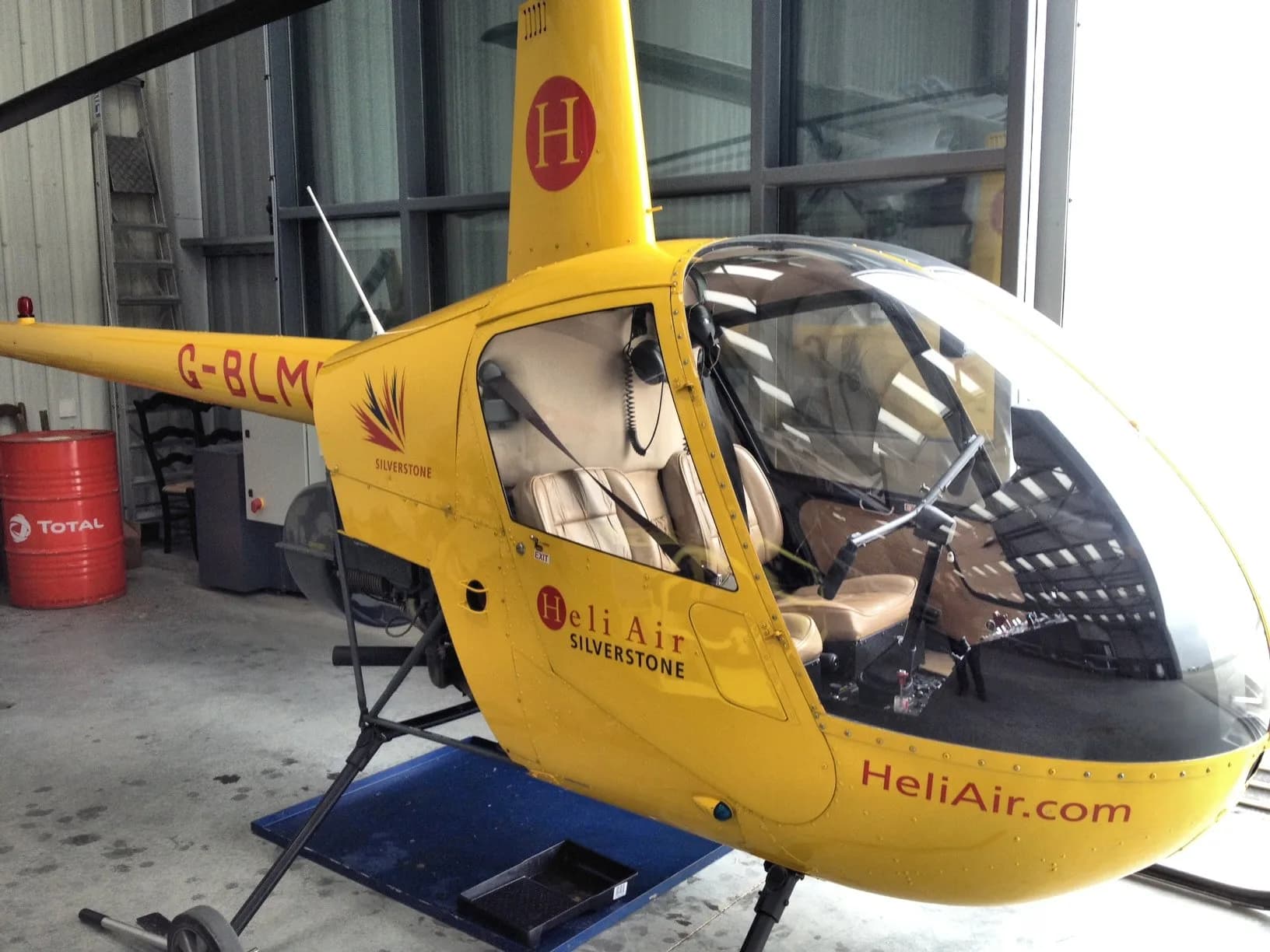 A yellow Robinson R44 helicopter with "HeliAir Silverstone" branding, parked in a hangar.