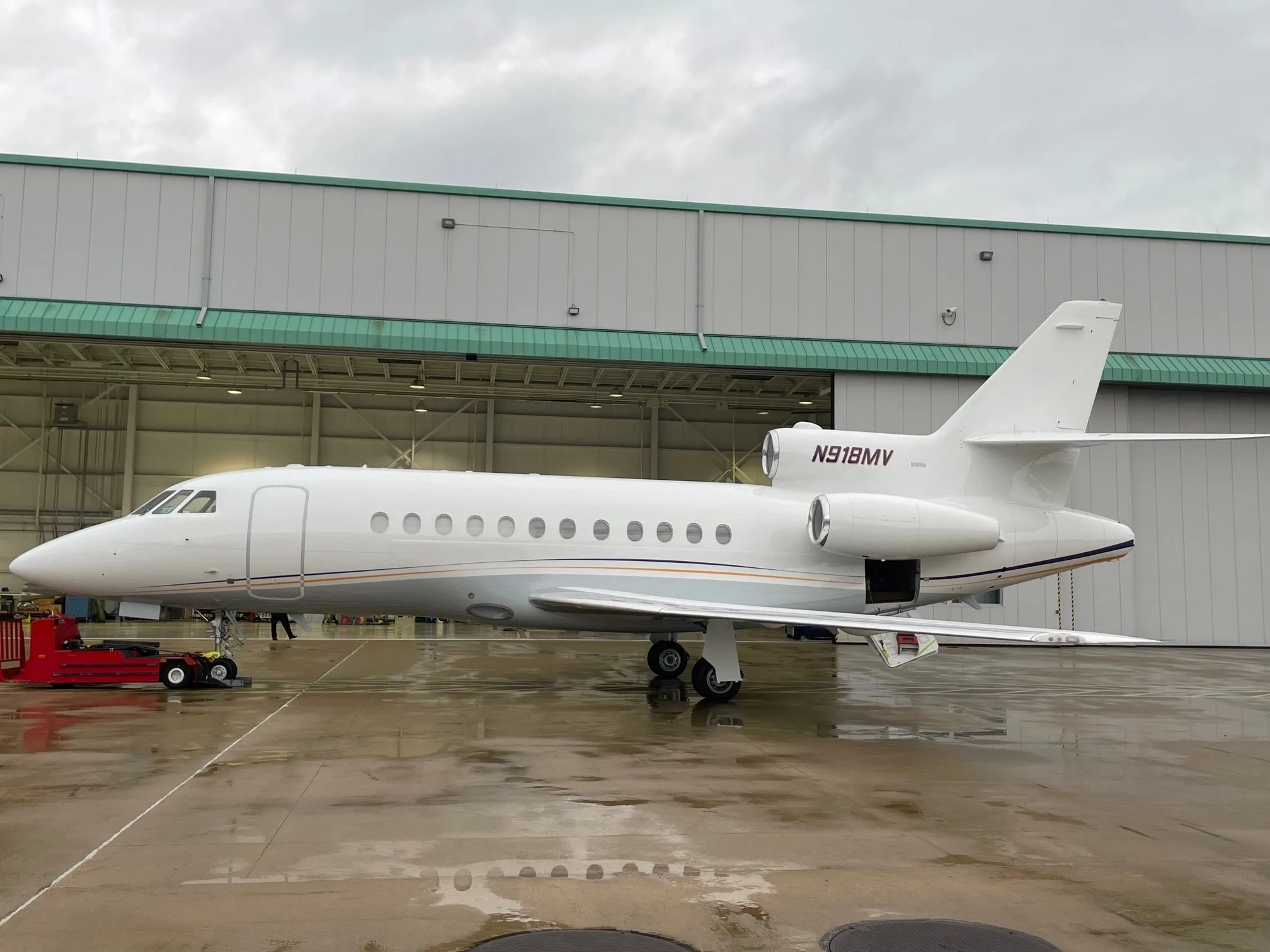 A Falcon aircraft with registration N918MV is parked outside a hangar.