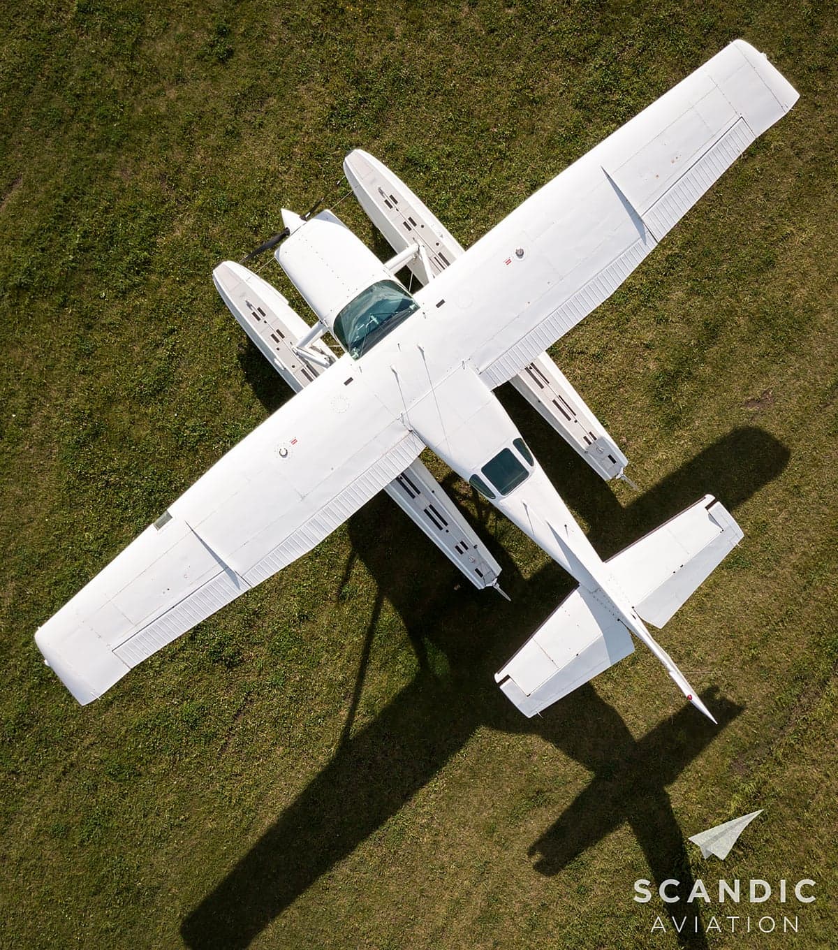 Aerial view of a white floatplane on a grassy field.