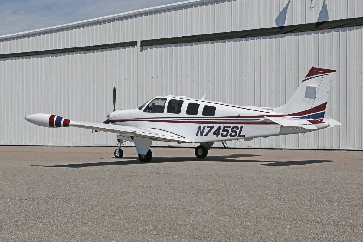 Side view of a white and red Beechcraft Bonanza aircraft with registration N745SL parked in front of a hangar.