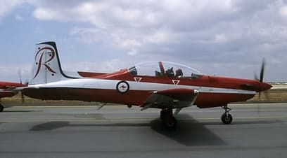 Side view of a red and white Pilatus PC-9 aircraft on the tarmac.