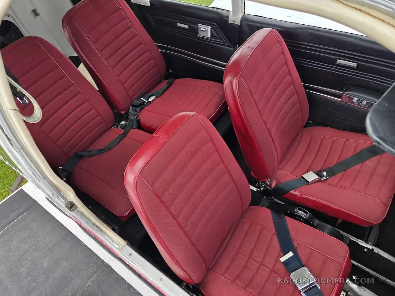 The interior of a Piper Cherokee aircraft showing four red fabric seats with seatbelts.