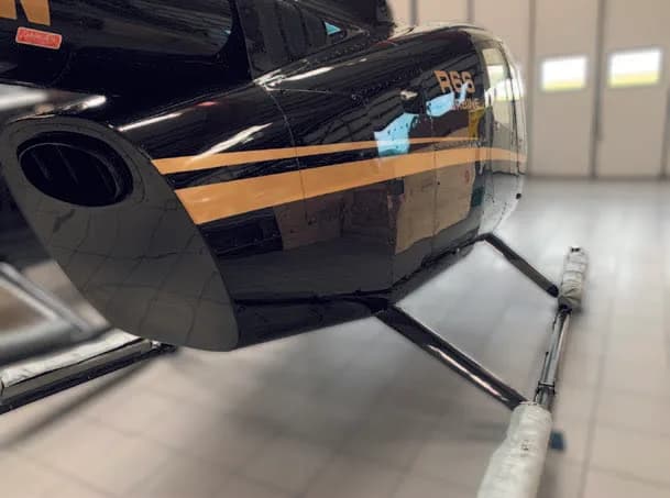 A close-up of the black tail section and exhaust of a Robinson R66 helicopter with a gold stripe.