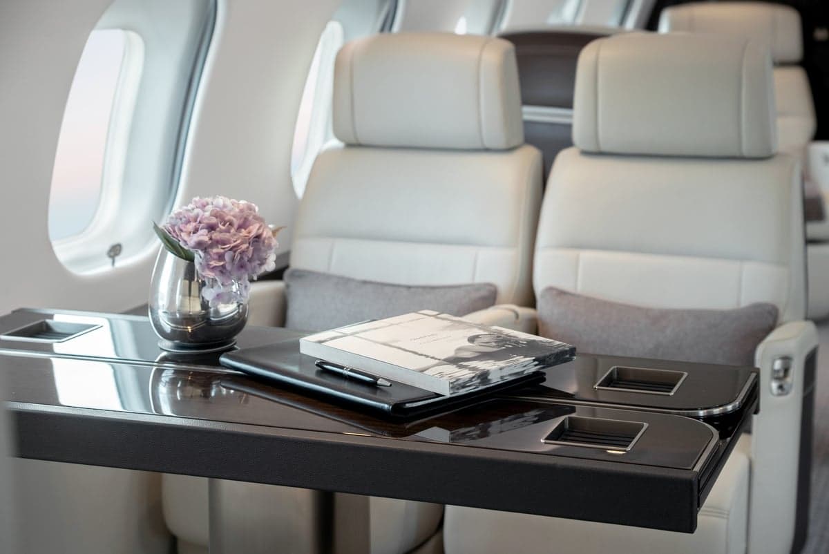 A table with a book and a vase of flowers between two white leather seats in the aircraft cabin.