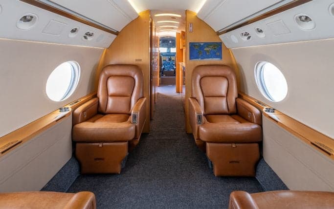 Aircraft cabin interior with a table, cabinets, and leather seats.