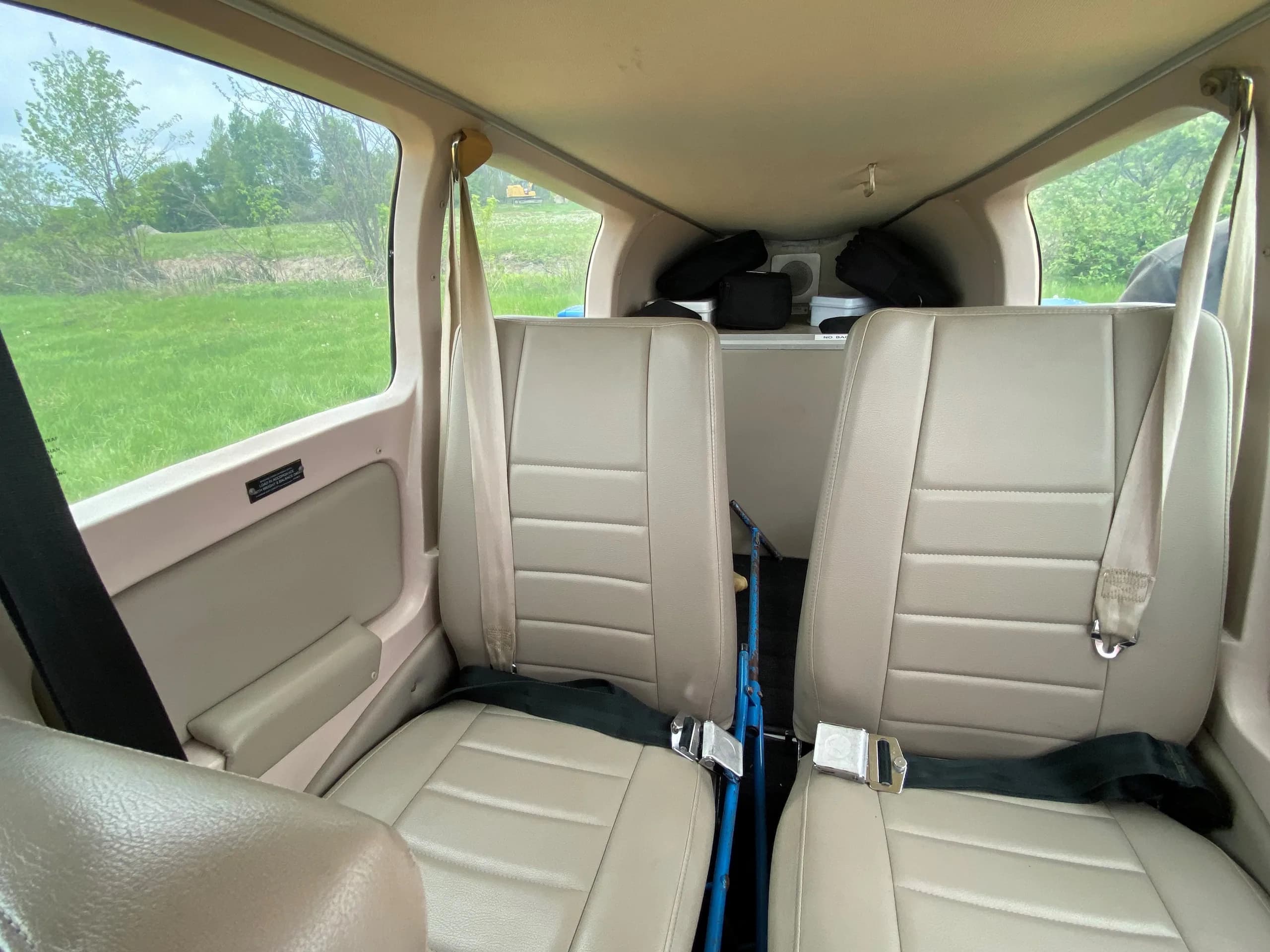 The rear cabin of the aircraft showing two beige seats with seatbelts and a view of green trees outside.
