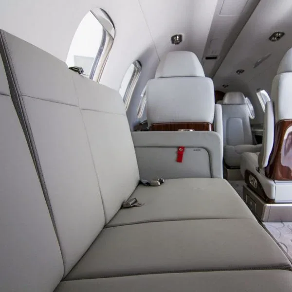 A private jet cabin interior showing a light grey divan seat next to a window.