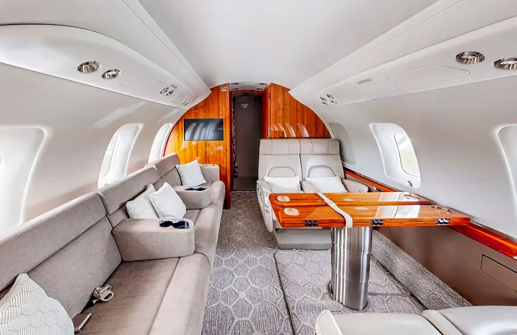 A private jet cabin interior featuring a comfortable lounge sofa and a dining table with wood finish.