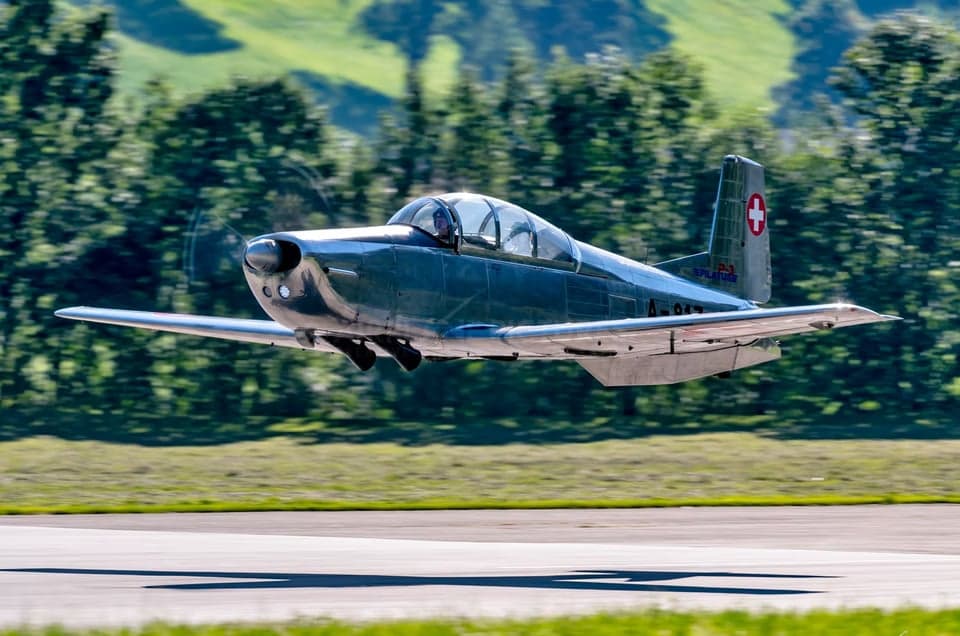 Two Pilatus PC-7 aircraft flying in formation over a wooded area.