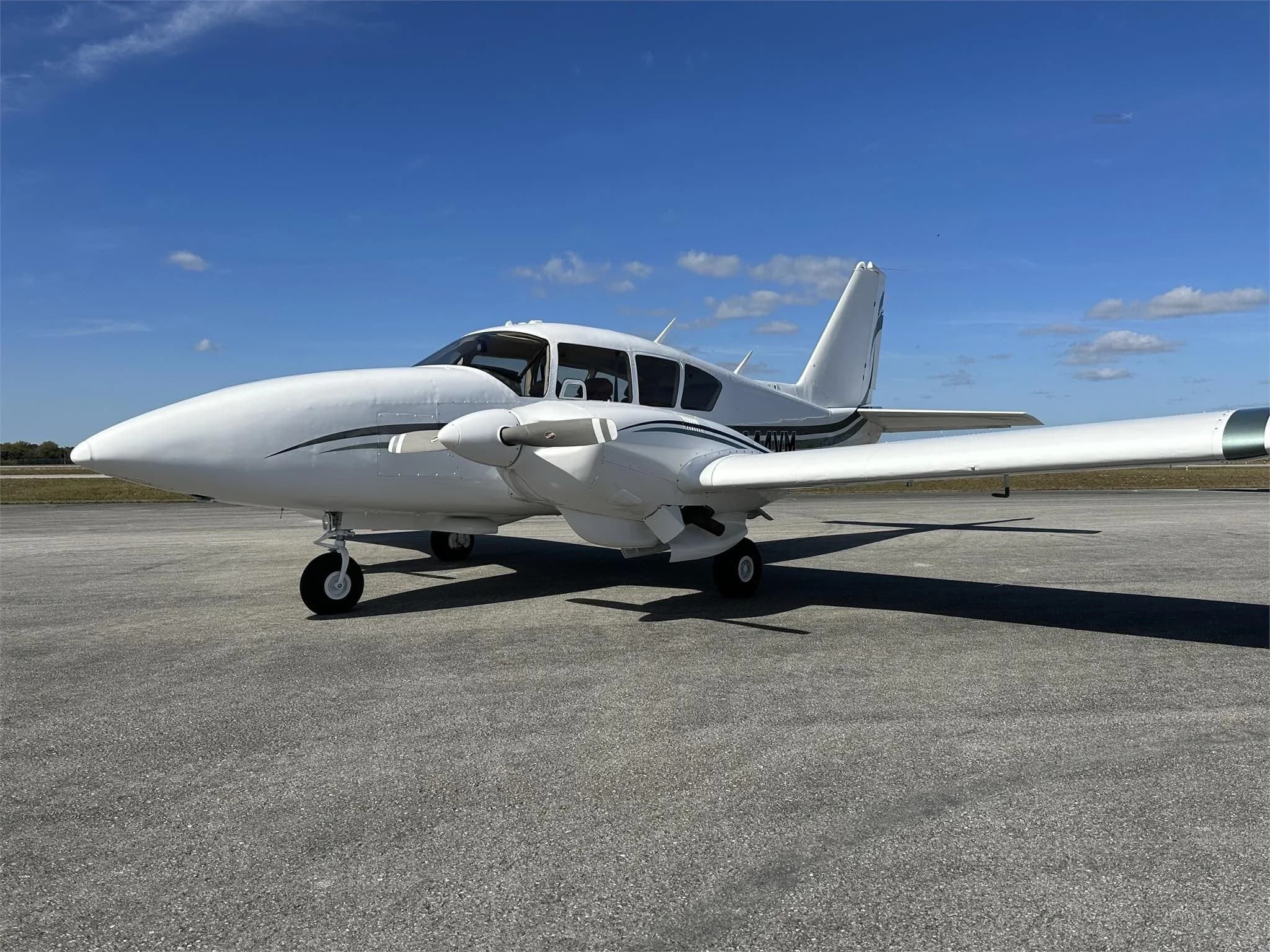A front-side view of a white Piper aircraft with green and black stripes, registration N444VM, parked on an airfield.