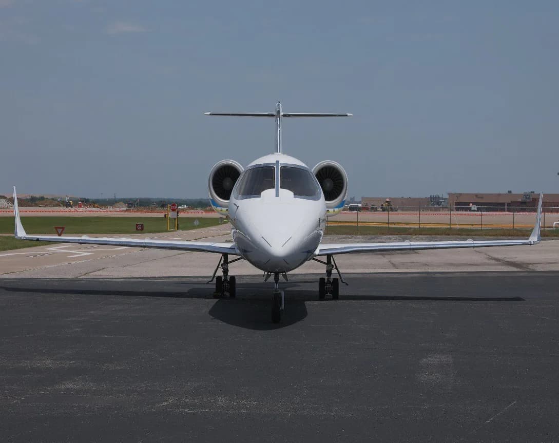 A white business jet with blue and yellow stripes, registration N75CT, viewed from the front on an asphalt tarmac.