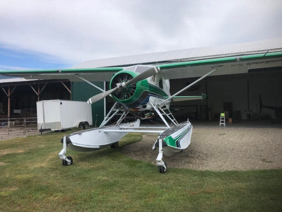 Front view of a green and white float plane parked in front of a hangar.
