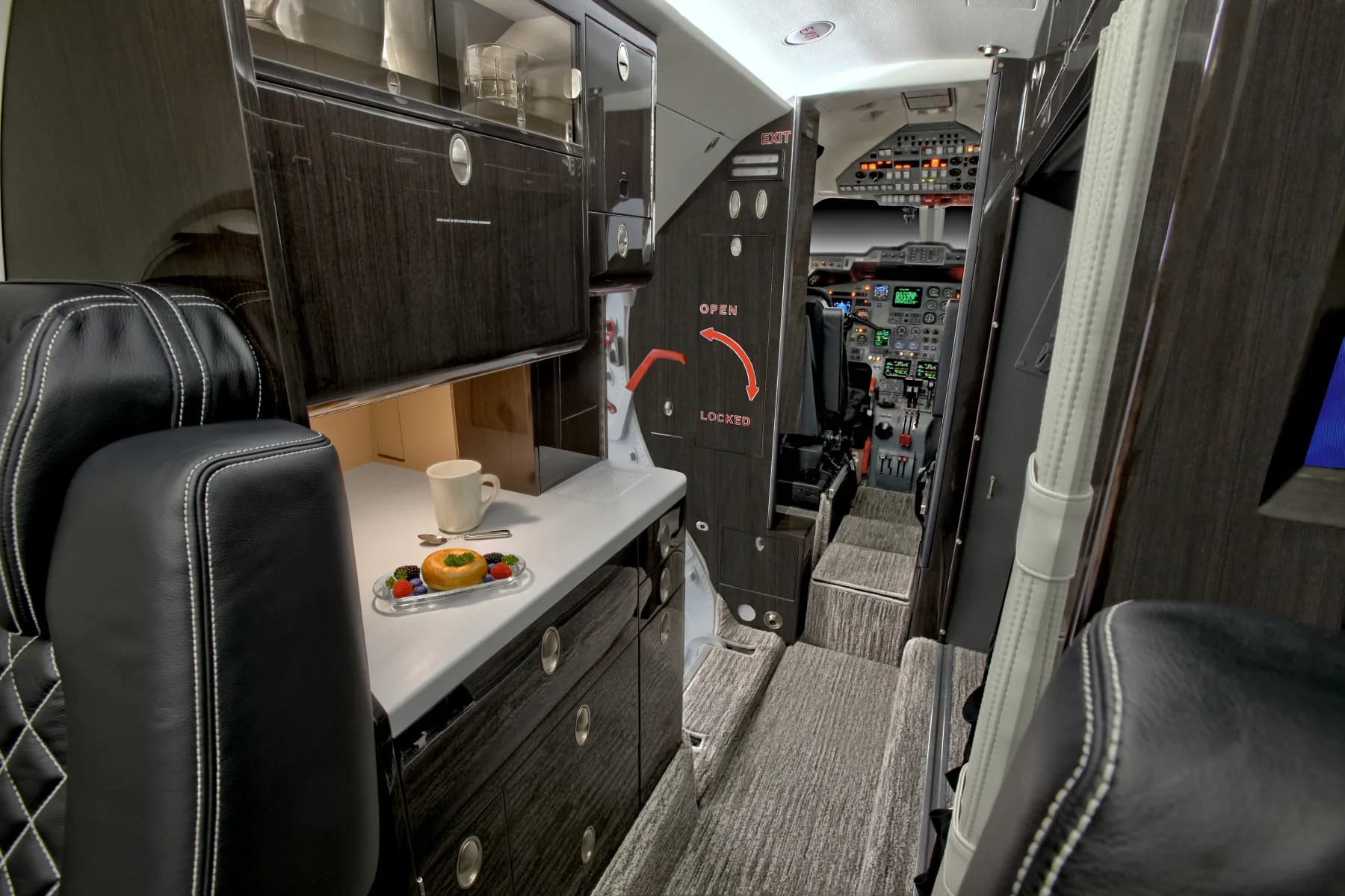 View of the aircraft galley and cockpit with black leather seats and wood accents.