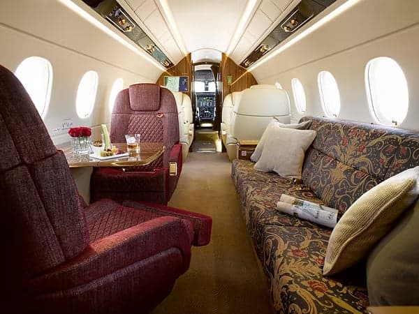 A view of the interior of the aircraft with a red sofa and cream-colored leather seats.