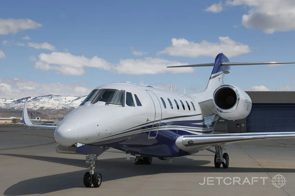 A close-up front view of a white and blue Cessna Citation X business jet parked on an airfield.