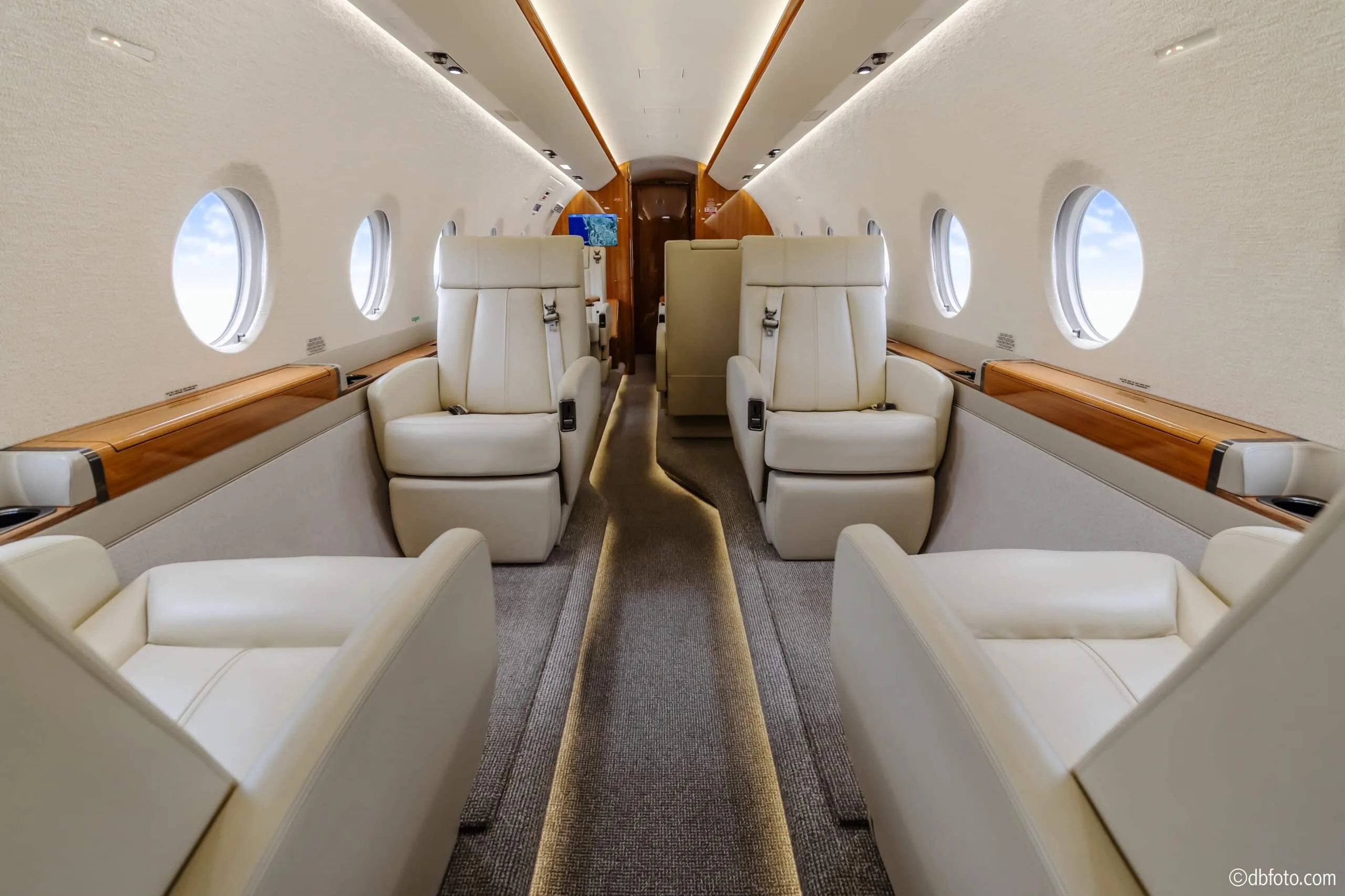 A view down the aircraft cabin aisle showing cream leather seats and large windows.