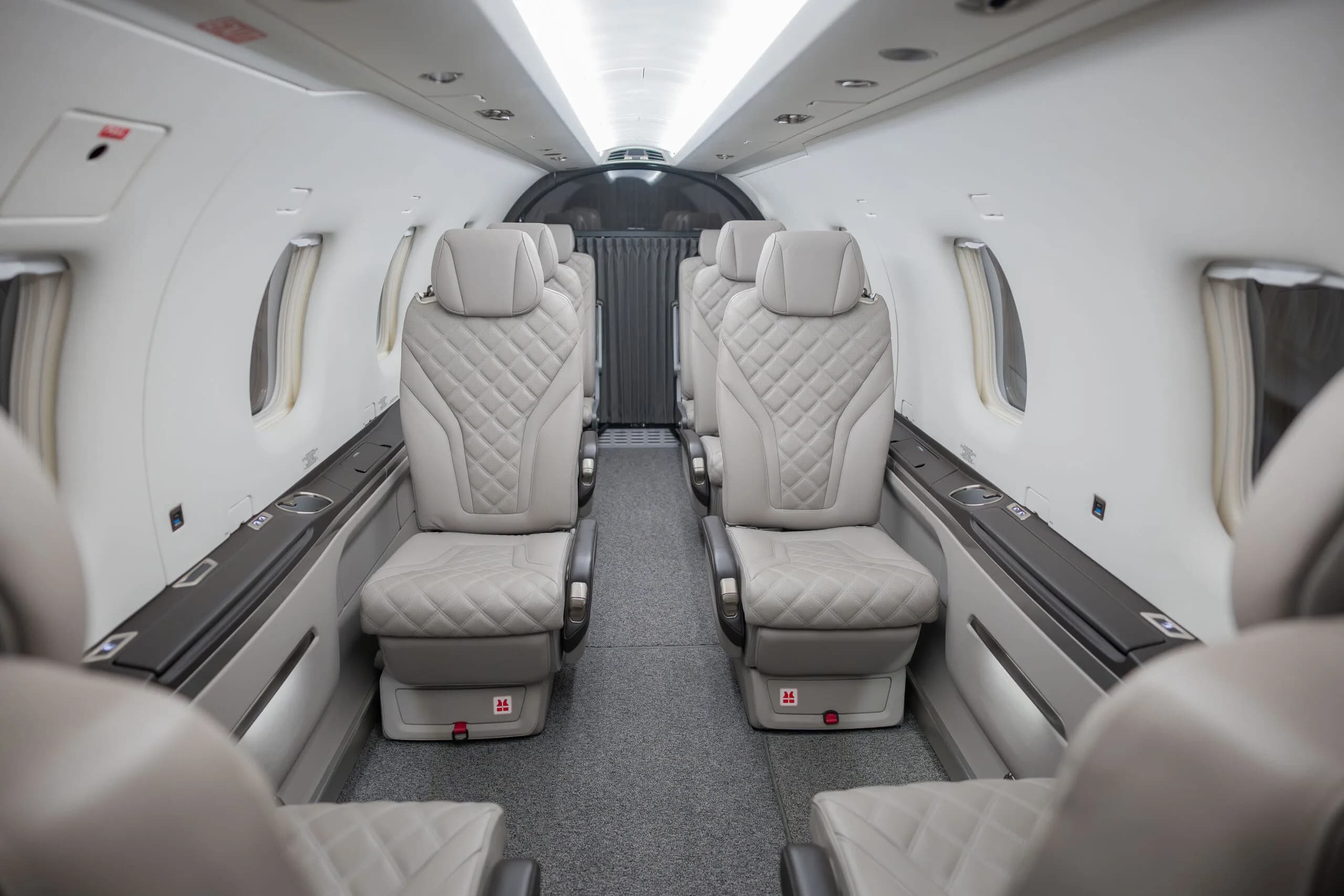 The light grey quilted leather seats of an aircraft cabin, viewed from the rear looking forward.