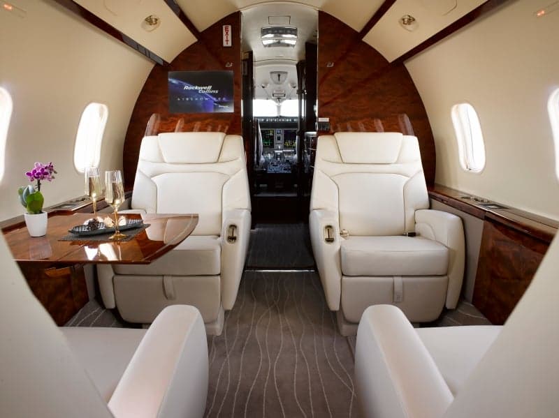 The aircraft's interior features white leather seats and wood accents.