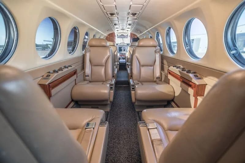 The aircraft cabin features tan leather seats arranged in a club configuration with round windows.