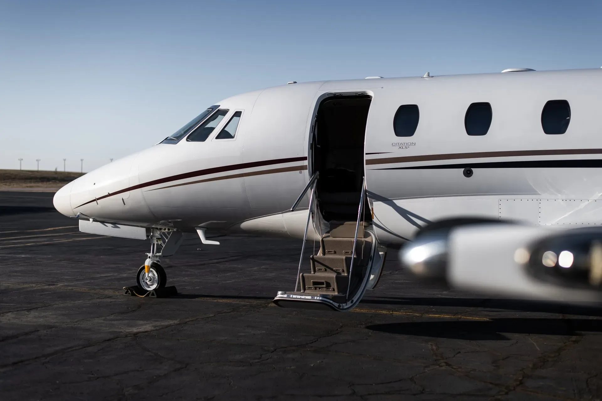 A white Citation XLS+ business jet is parked on the tarmac with the airstair door open.