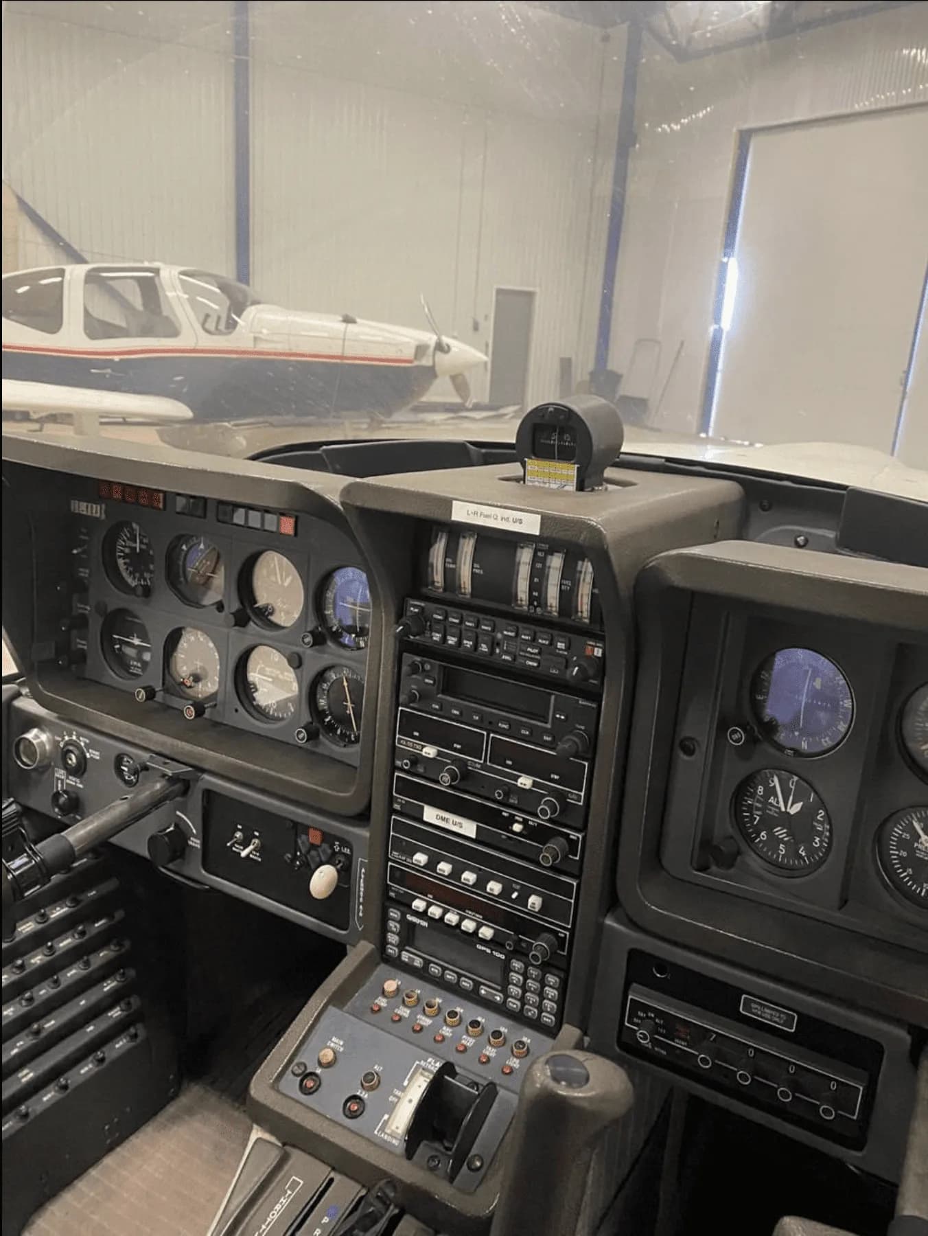 View from inside the cockpit showing the instrument panel and another aircraft in the hangar through the windshield.
