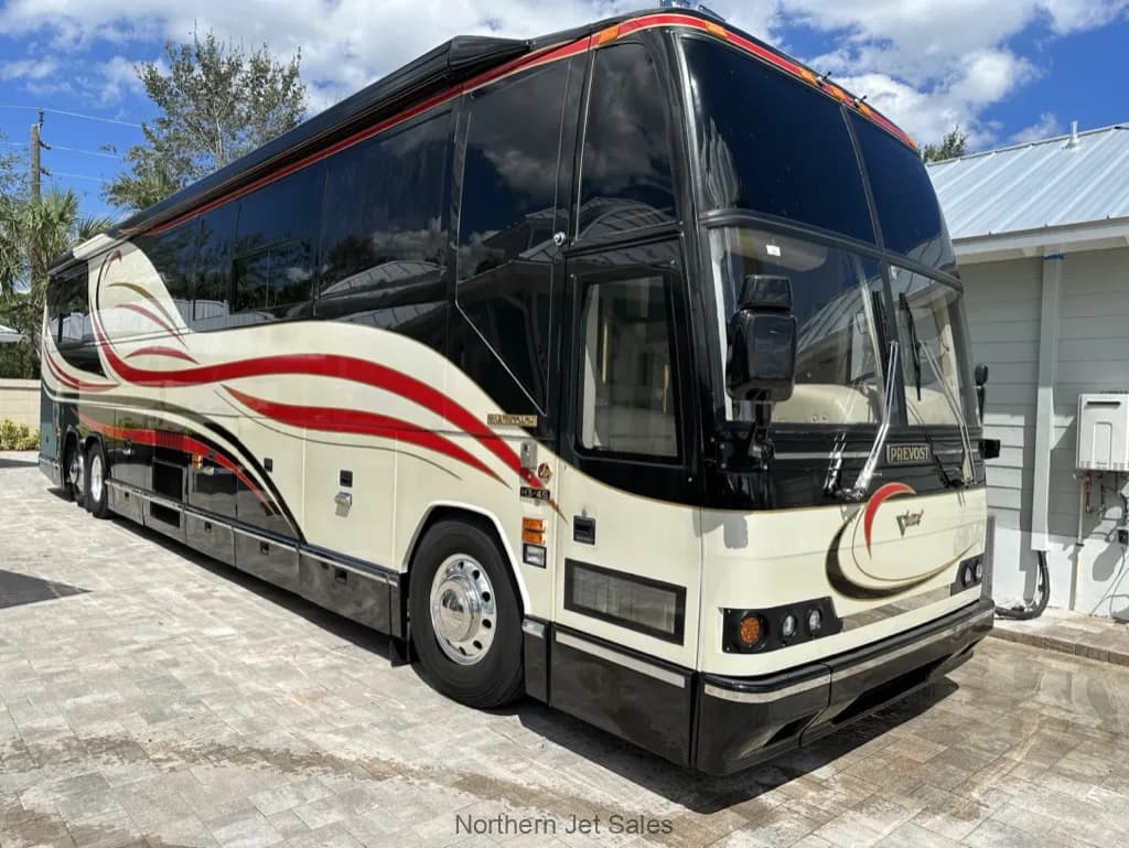 Front side view of a Prevost coach with a black, white, and red paint scheme parked outside.