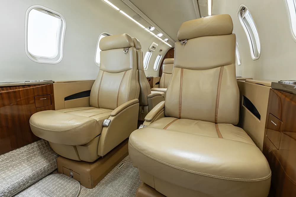 Close-up view of tan leather seats in a private jet cabin with wood paneling.