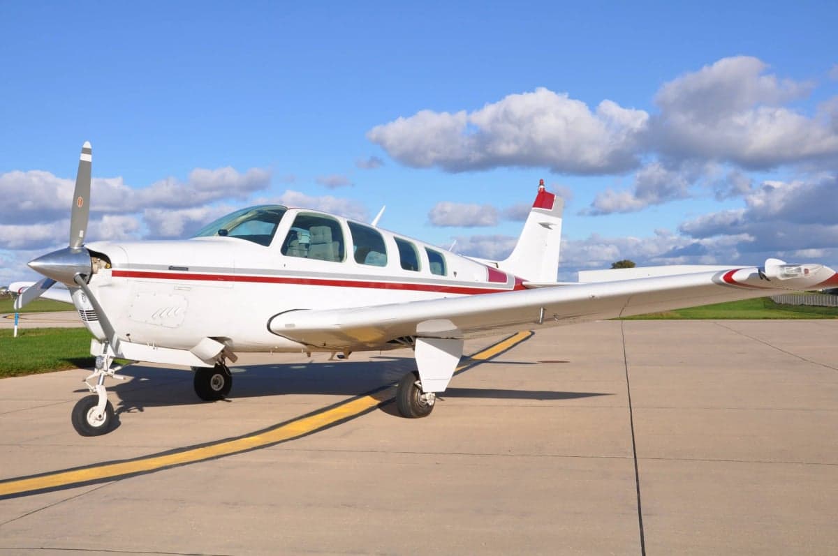 A Beechcraft Bonanza aircraft with a red and white paint scheme, parked on the tarmac.