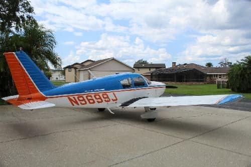 A Piper Archer aircraft with tail number N9699J parked on a concrete surface with a blue sky background.