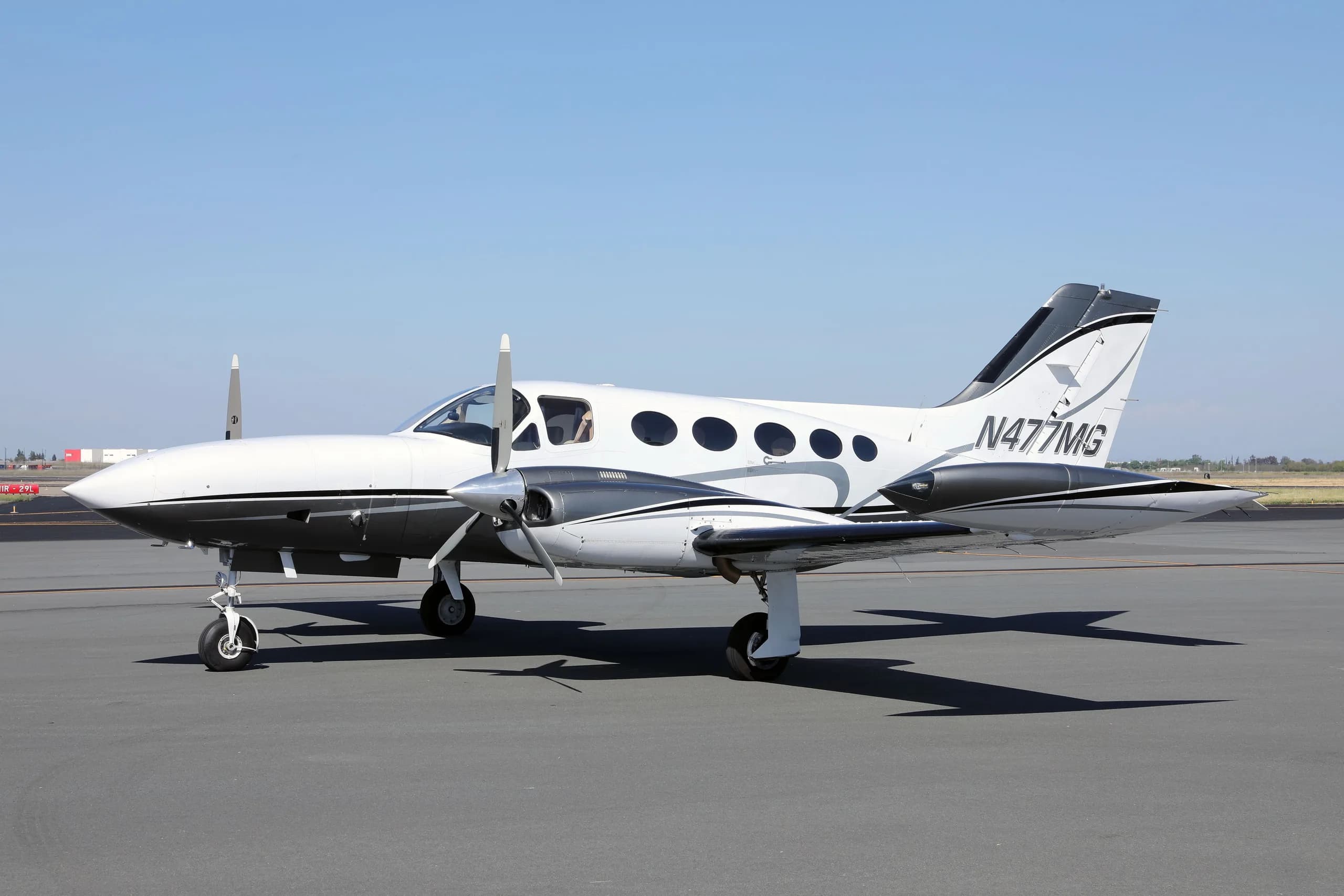 A white and grey twin-engine Cessna 414 Chancellor aircraft, N477MG, parked on an asphalt tarmac under a clear sky.