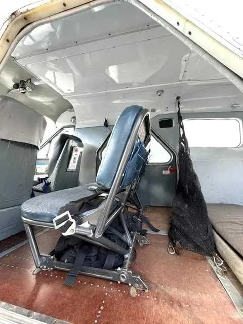 The interior cabin of an aircraft showing a single blue seat with harnesses and a dark cargo net.