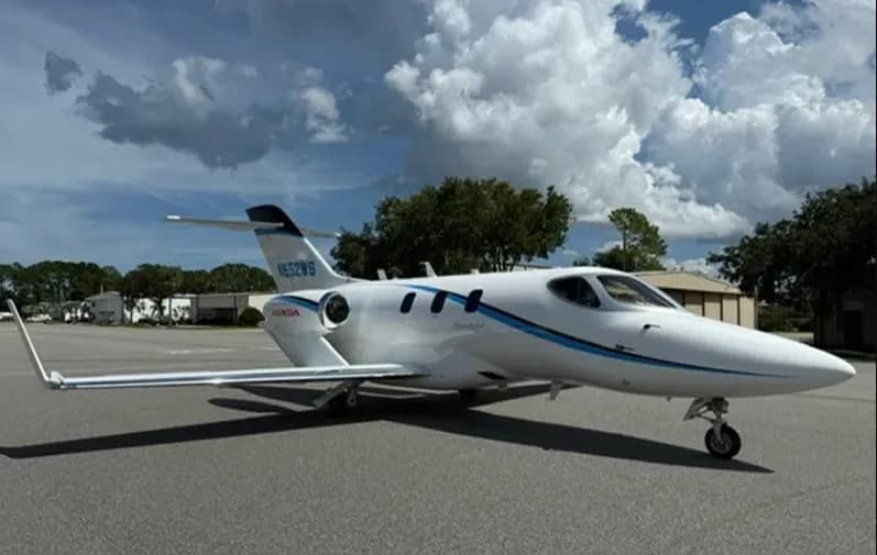 A white HondaJet HA-420 with blue accent stripes, registration N552WS, parked on an airfield under a partly cloudy sky.