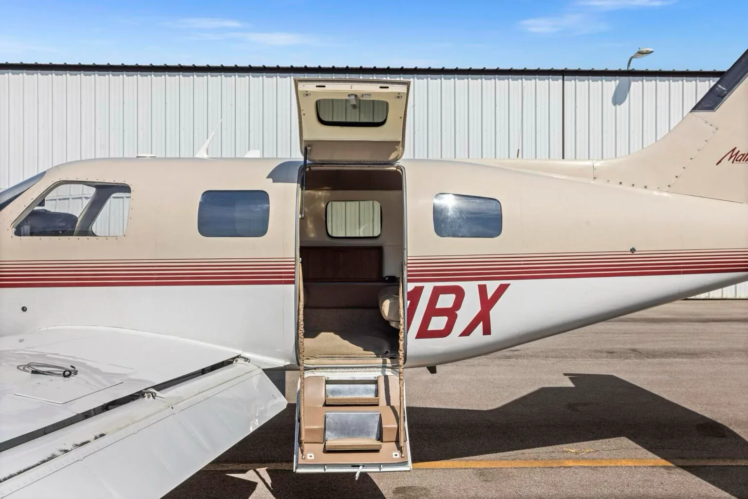 A side view of the Piper Malibu N31BX with its passenger door open, revealing the interior steps.