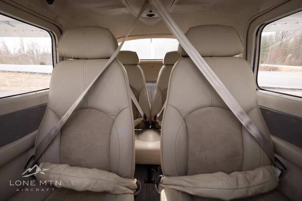 The light tan leather interior of an aircraft cabin, showing two front seats with seatbelts.