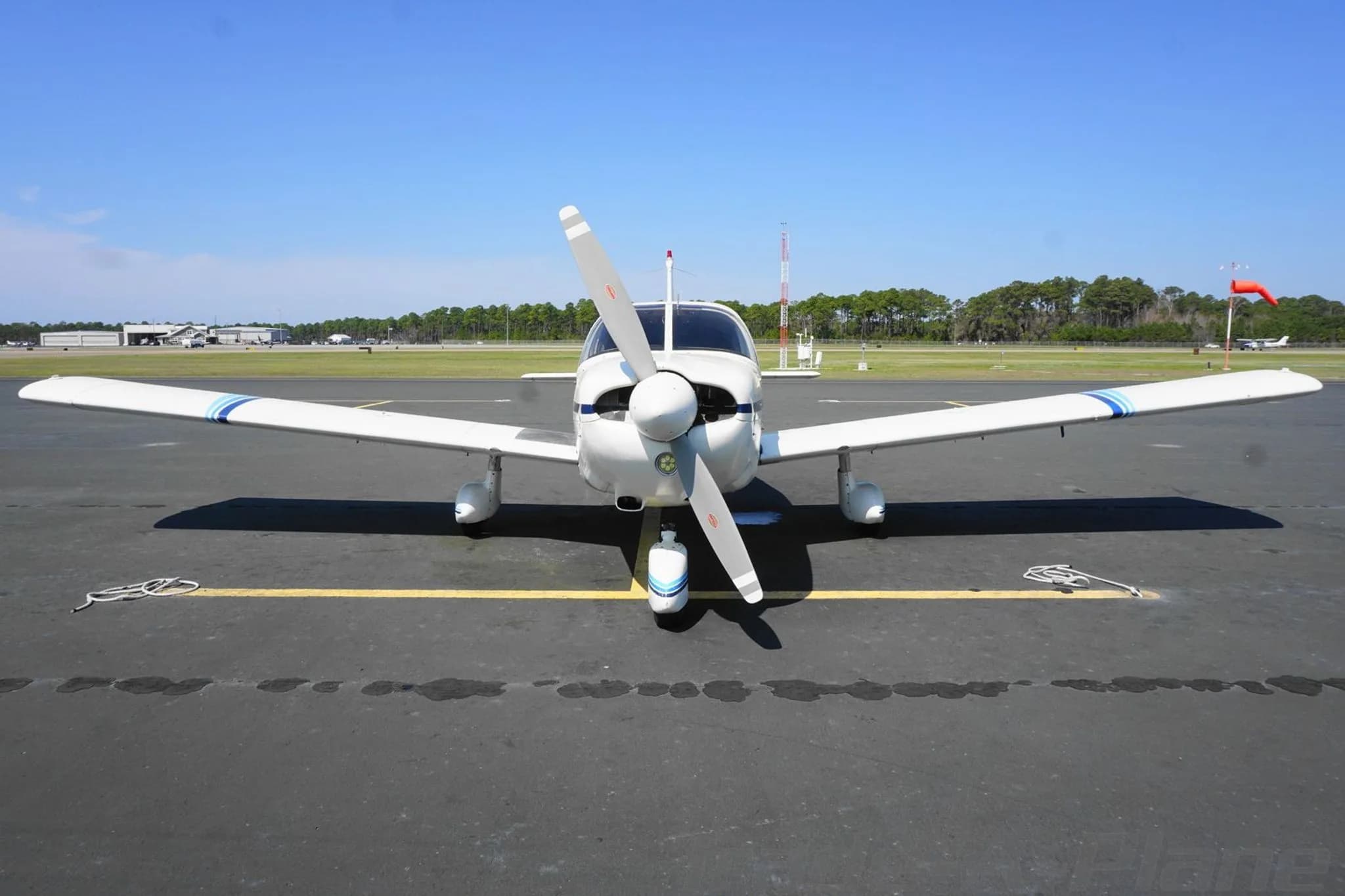 Front view of a white single-engine propeller aircraft with blue stripes parked on an airport tarmac.