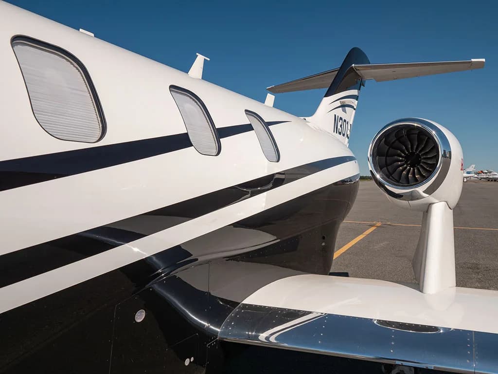 A close-up of the rear fuselage, over-wing engine, and tail of a white and black HondaJet N301JT on the tarmac.