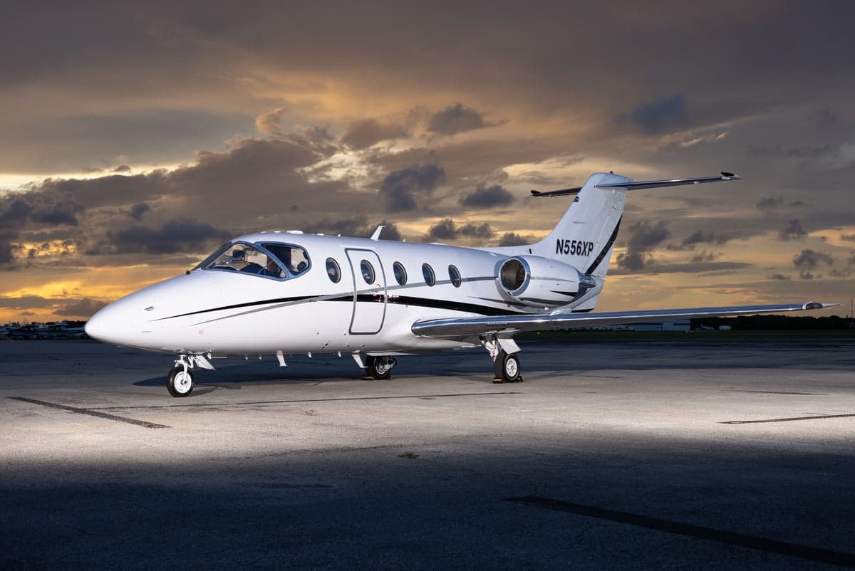 A white Learjet sits on the tarmac in the evening light.
