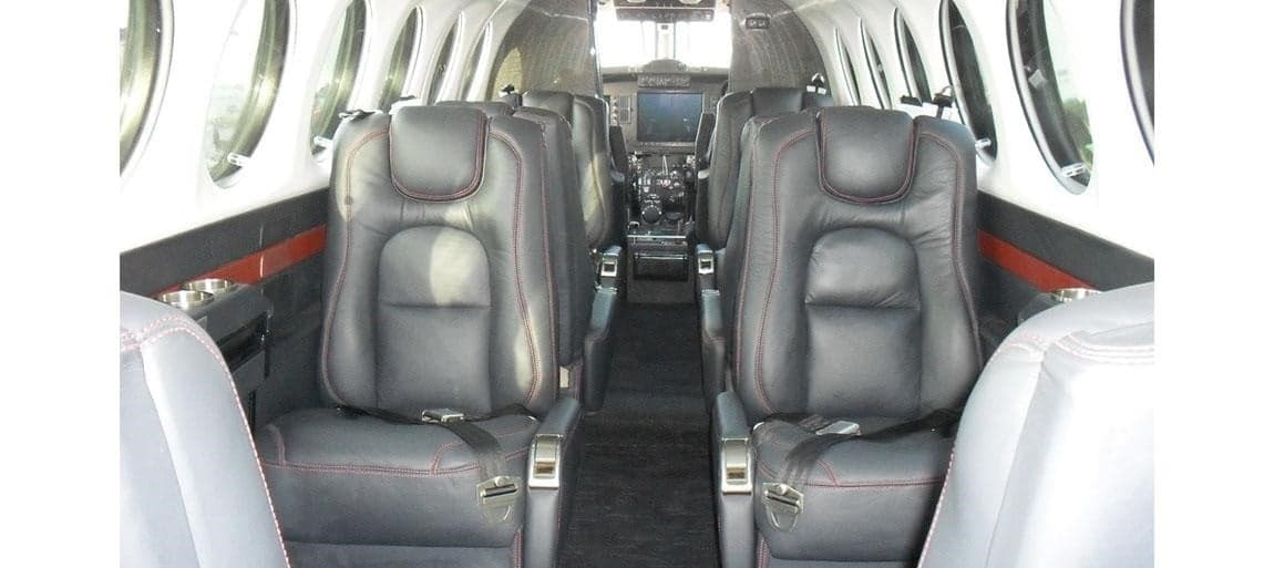 The interior of the Beechcraft King Air 350 features black leather seats with red stitching and a view towards the cockpit.