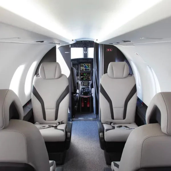 An aircraft cabin interior with grey and black seats, looking towards a modern glass cockpit.
