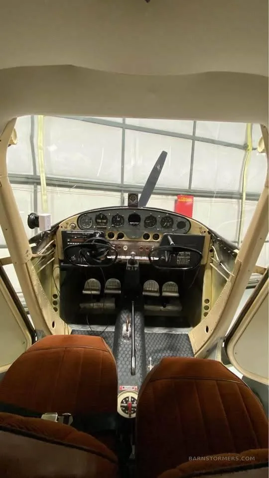 Wide view of an aircraft cockpit, showing the instrument panel, control yokes, and two brown seats.